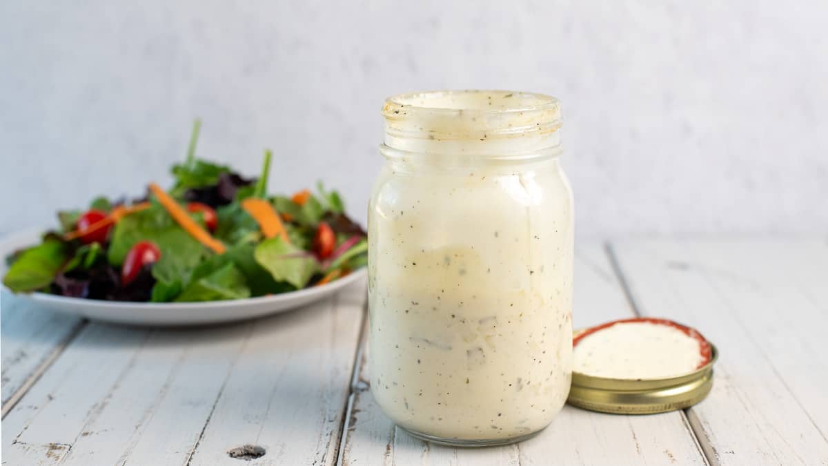 dill pick ranch dressing in a mason jar with a salad in the background