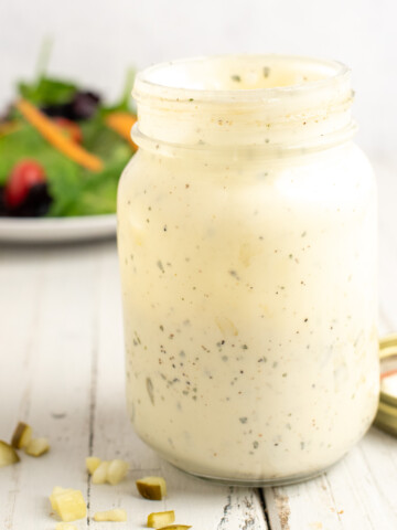 ranch in a mason jar with dill pickles scattered around