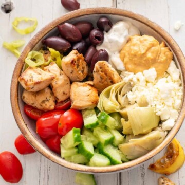 Greek chicken bowl with tomatoes, kalamata olives, and chicken scattered around.