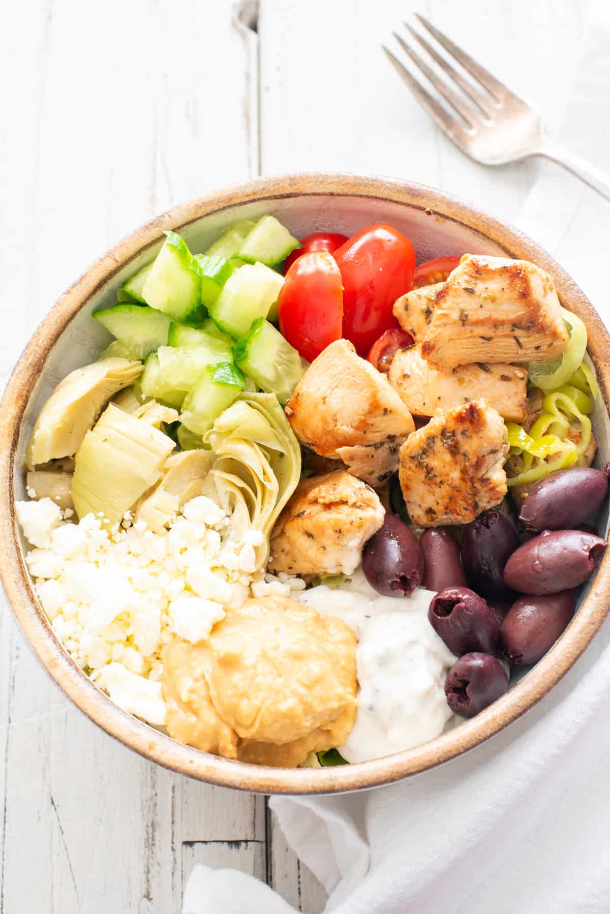 Greek chicken bowl on white background with fork nearby.