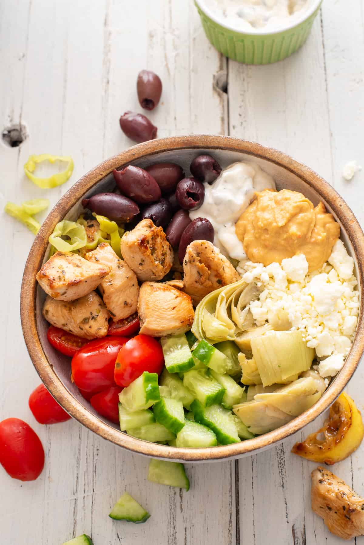Greek chicken bowl with tomatoes, kalamata olives, and chicken scattered around.