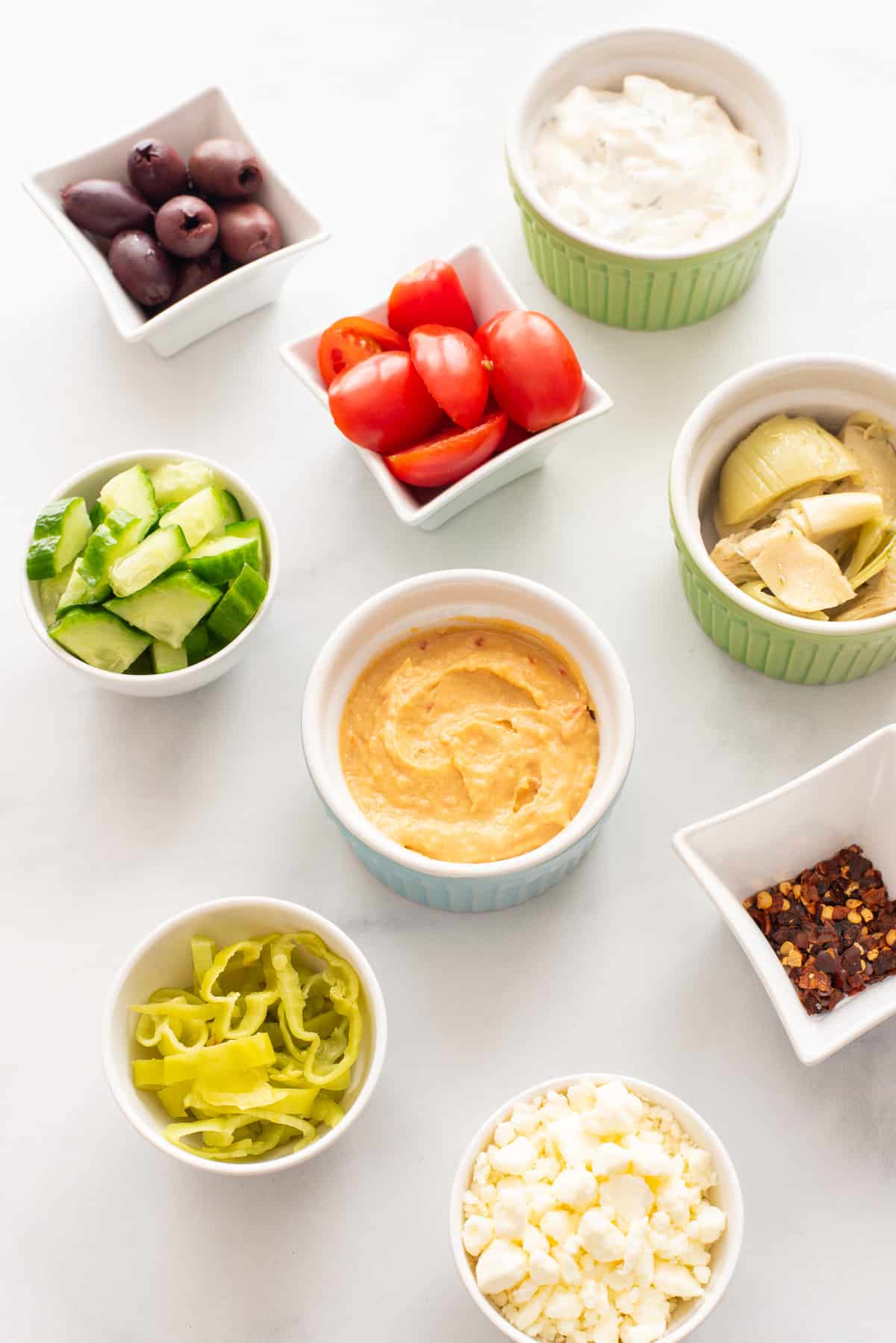 Ingredients needed for Greek chicken bowls in in individual bowls on a white background.