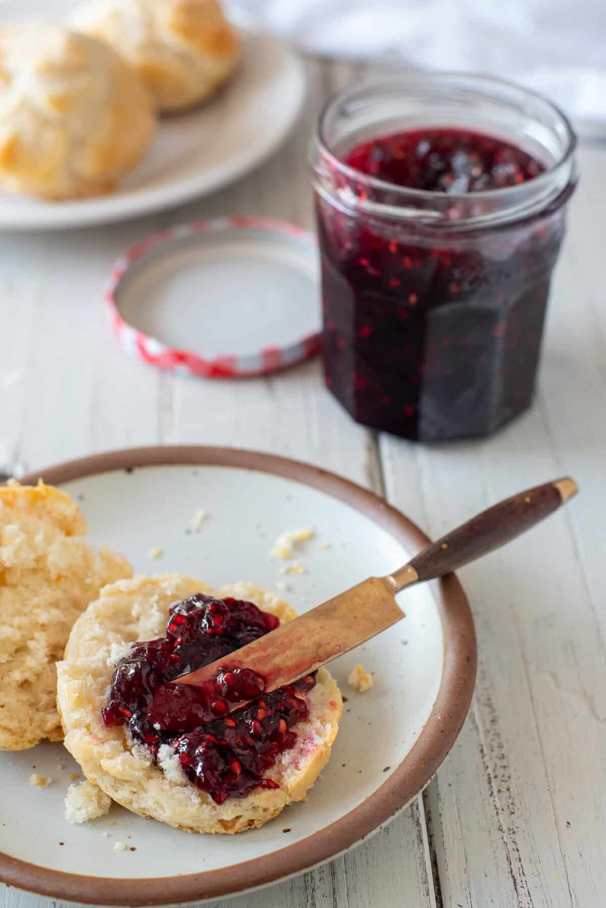 white plates on a white table with biscuits. The plate in the forefront has a biscuits sliced open with blackberry jam spread on it.