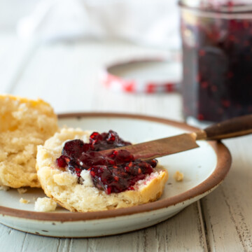 blackberry freezer jam spread on a split biscuits with a knife and a jar of jam in the background