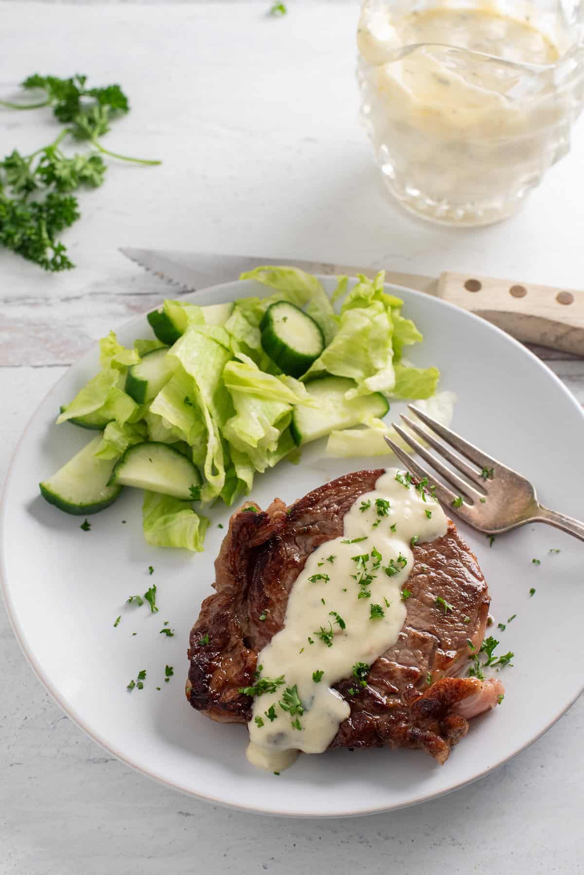 steak covered in gorgonzola cream sauce on a white plate with a green salad and a fork.