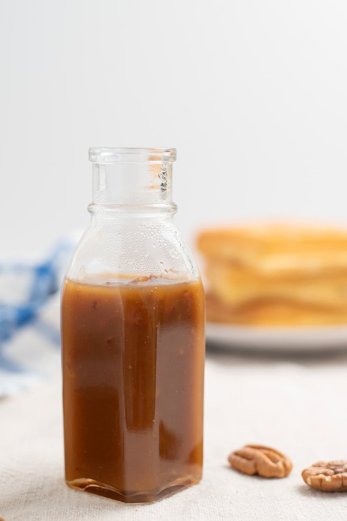 a glass bottle of butter pecan syrup with pecan halves laying nearby