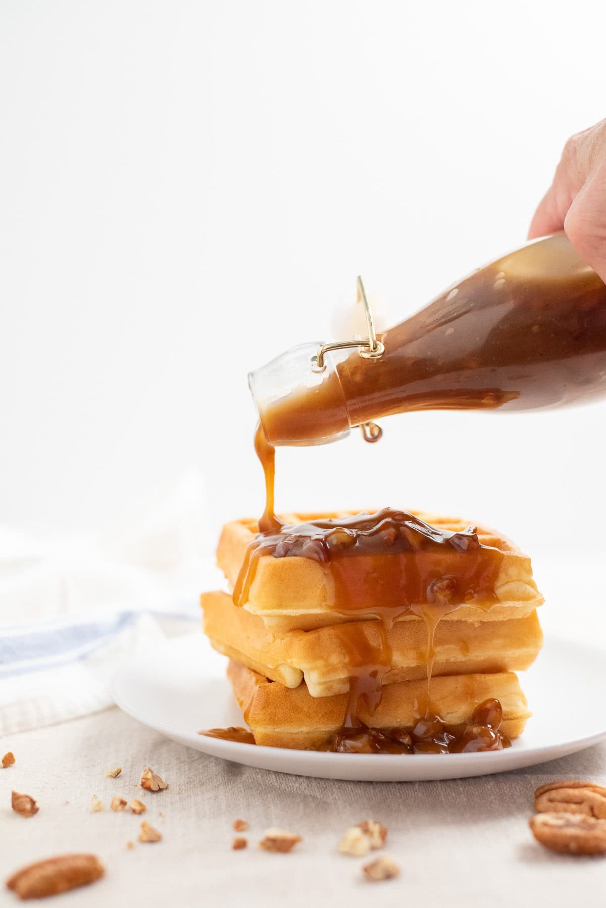 homemade butter pecan syrup being poured over a stack of fluffy Belgian waffles