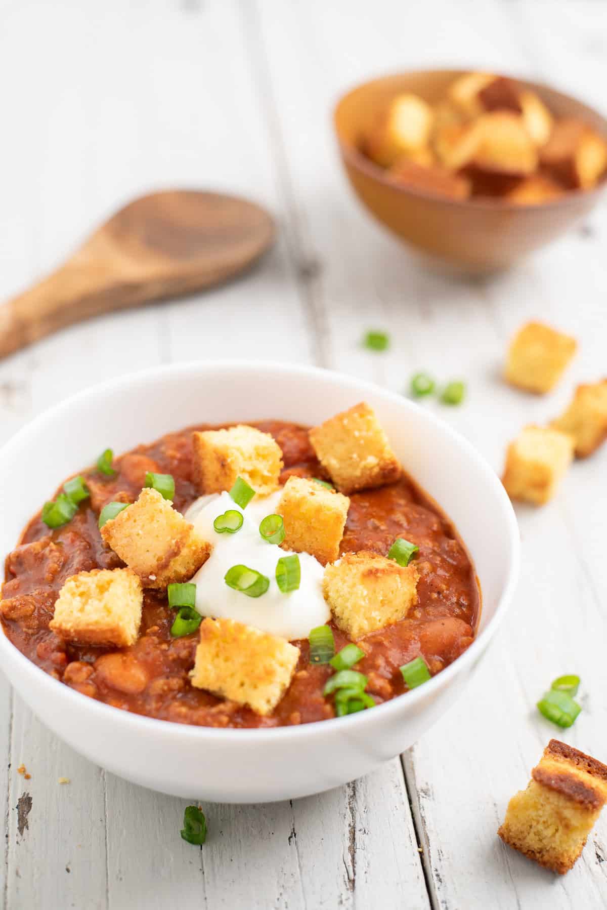 a white bowl of chili topped with cornbread croutons
