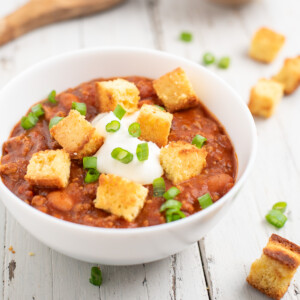 a white bowl of chili topped with cornbread croutons