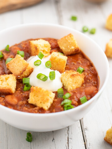a white bowl of chili topped with cornbread croutons