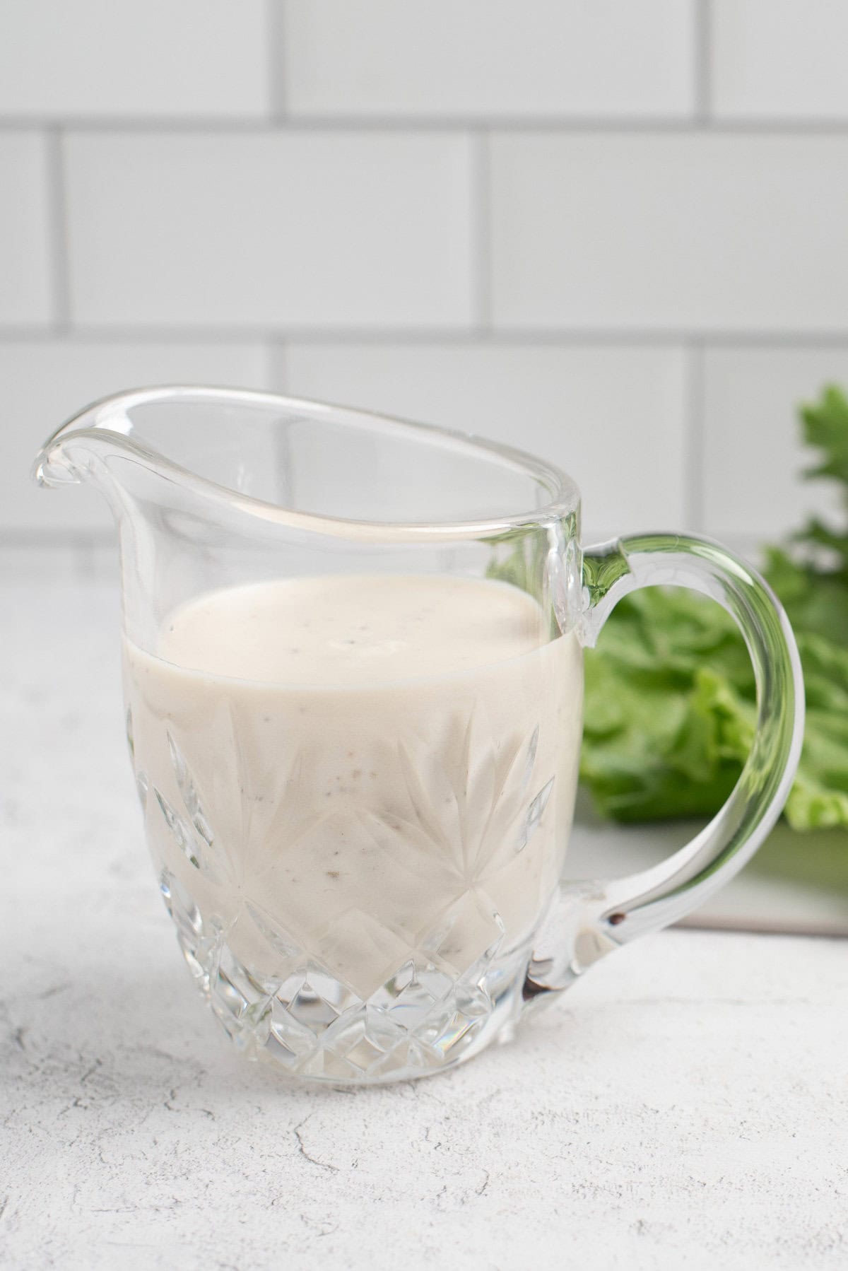greek salad dressing with yogurt in container with lettuce behind.