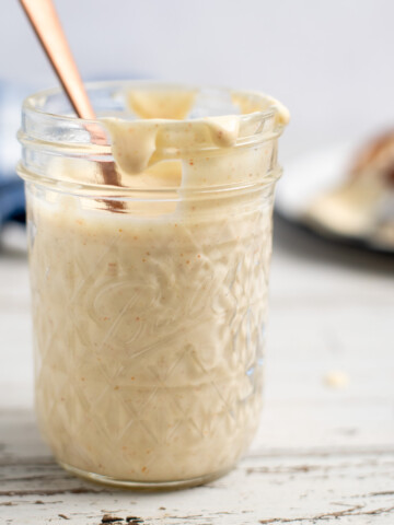 Alabama White BBQ Sauce in a glass jar with a gold spoon.
