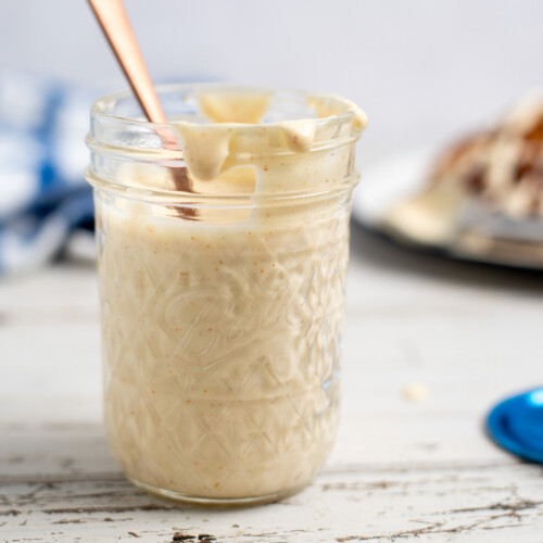 Alabama White BBQ Sauce in a glass jar with a gold spoon.