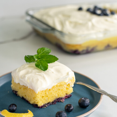 lemon blueberry poke cake topped with fresh mint on a blue plate