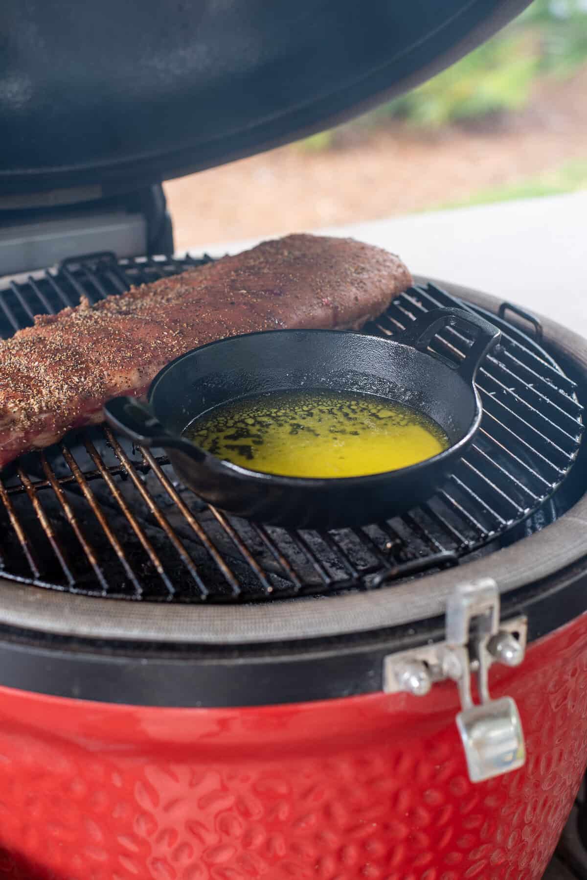 small skillet of butter on smoker next to ribs.