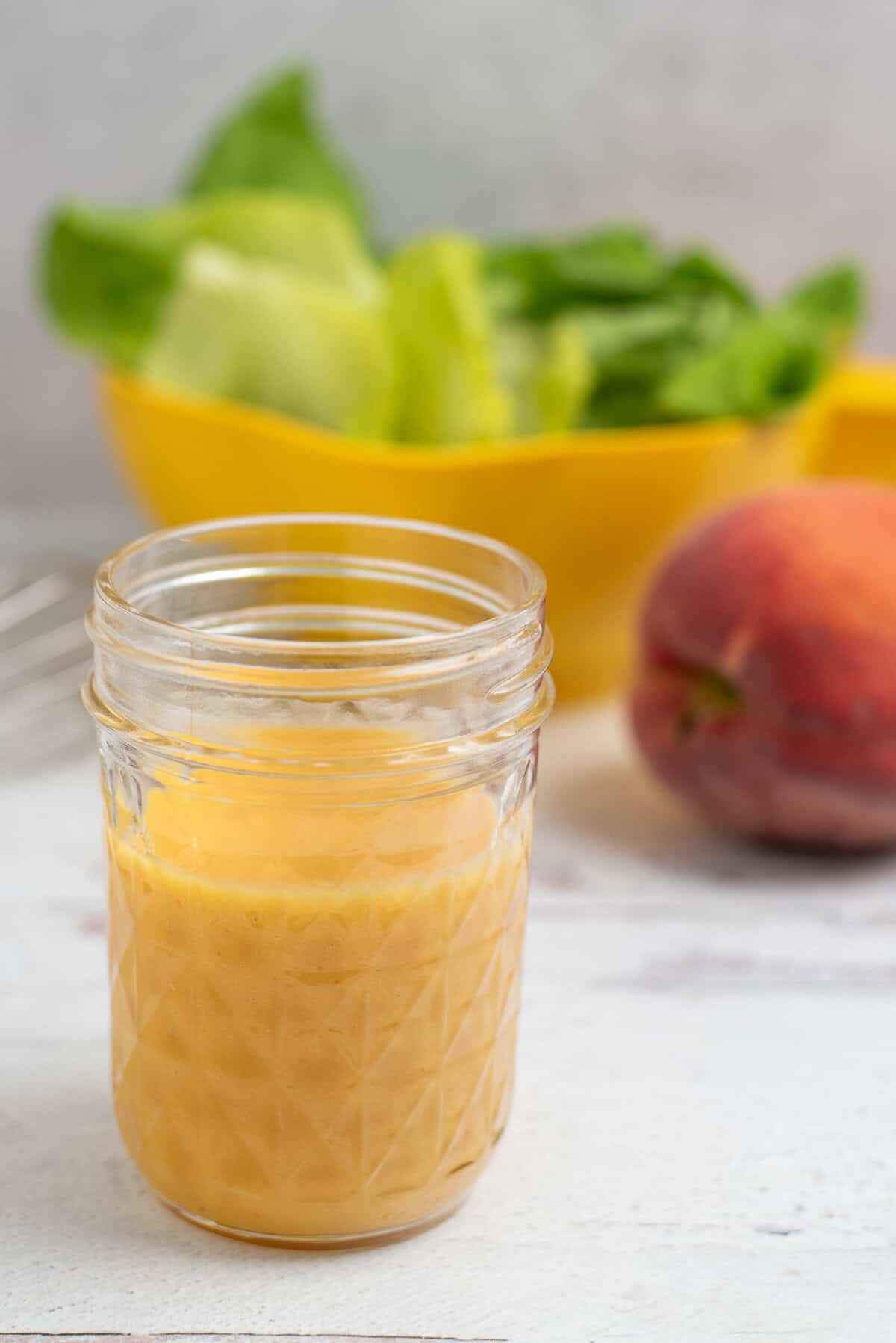 peach vinaigrette in a glass jar with salad ingredients behind it
