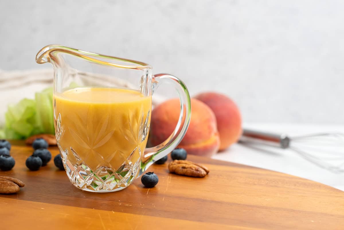 peach vinaigrette on a cutting board with fruits and vegetables in background
