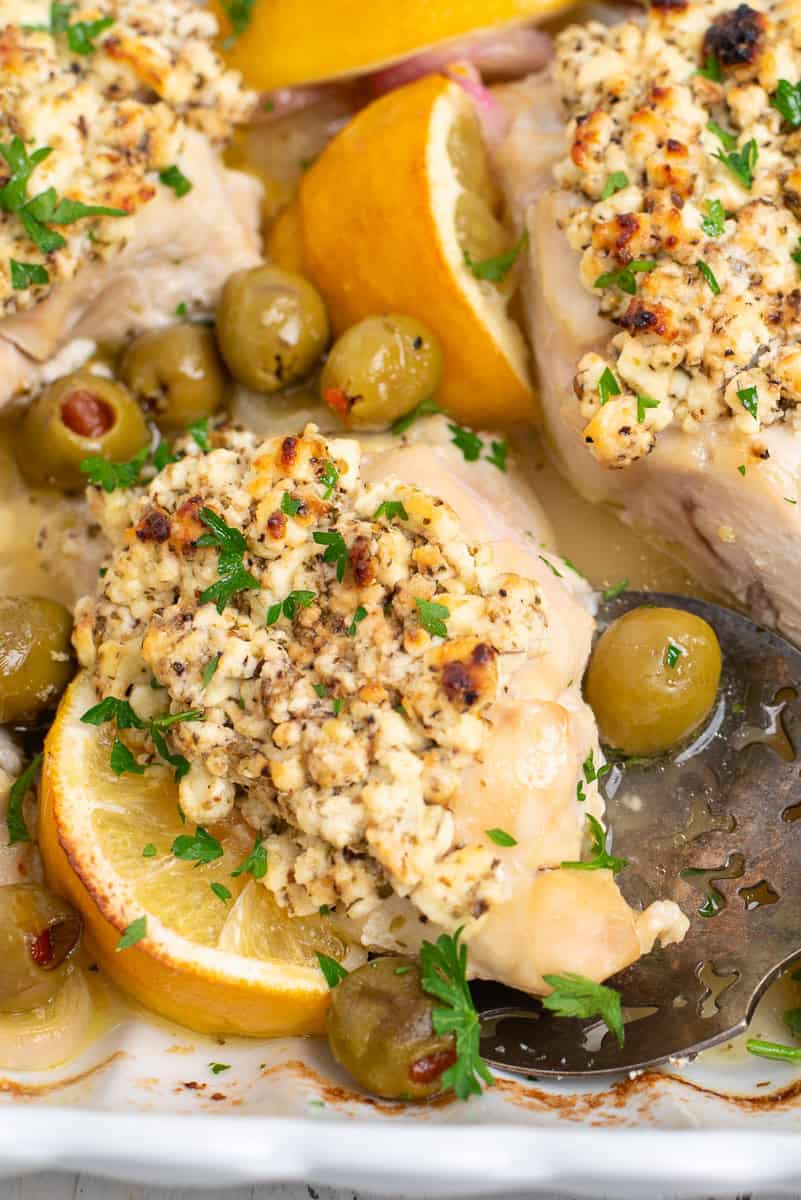 chicken topped with feta cheese, surrounded by olives, shallots, and lemon wedges