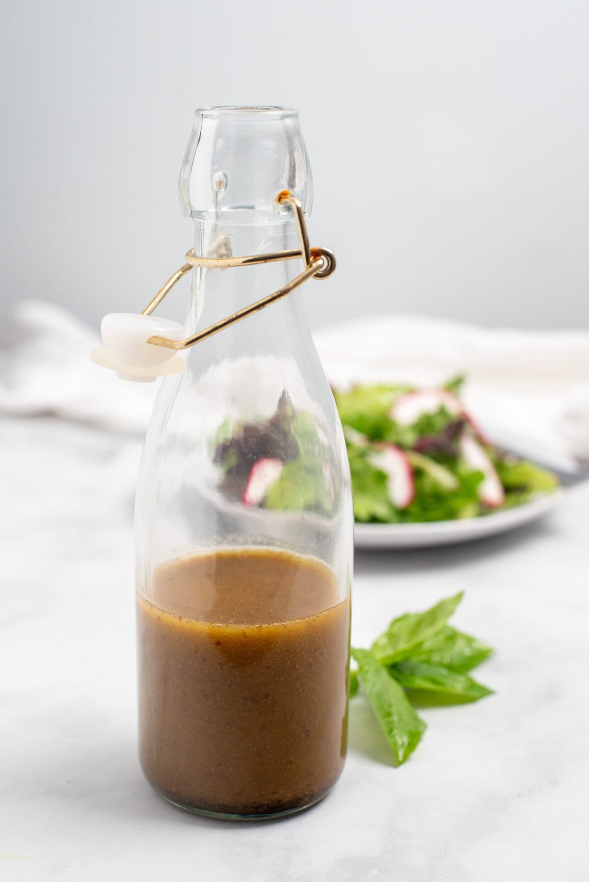 Balsamic Basil Vinaigrette in bottle with salad behind.