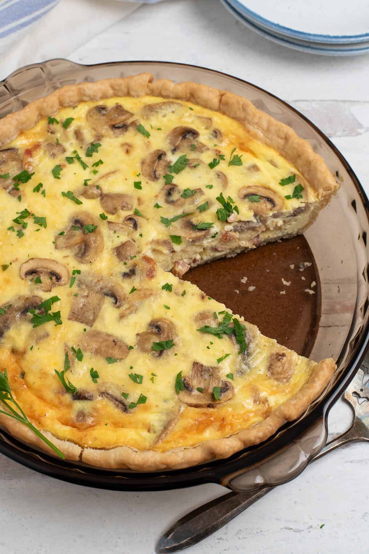 bacon and mushroom quiche with a slice missing.
