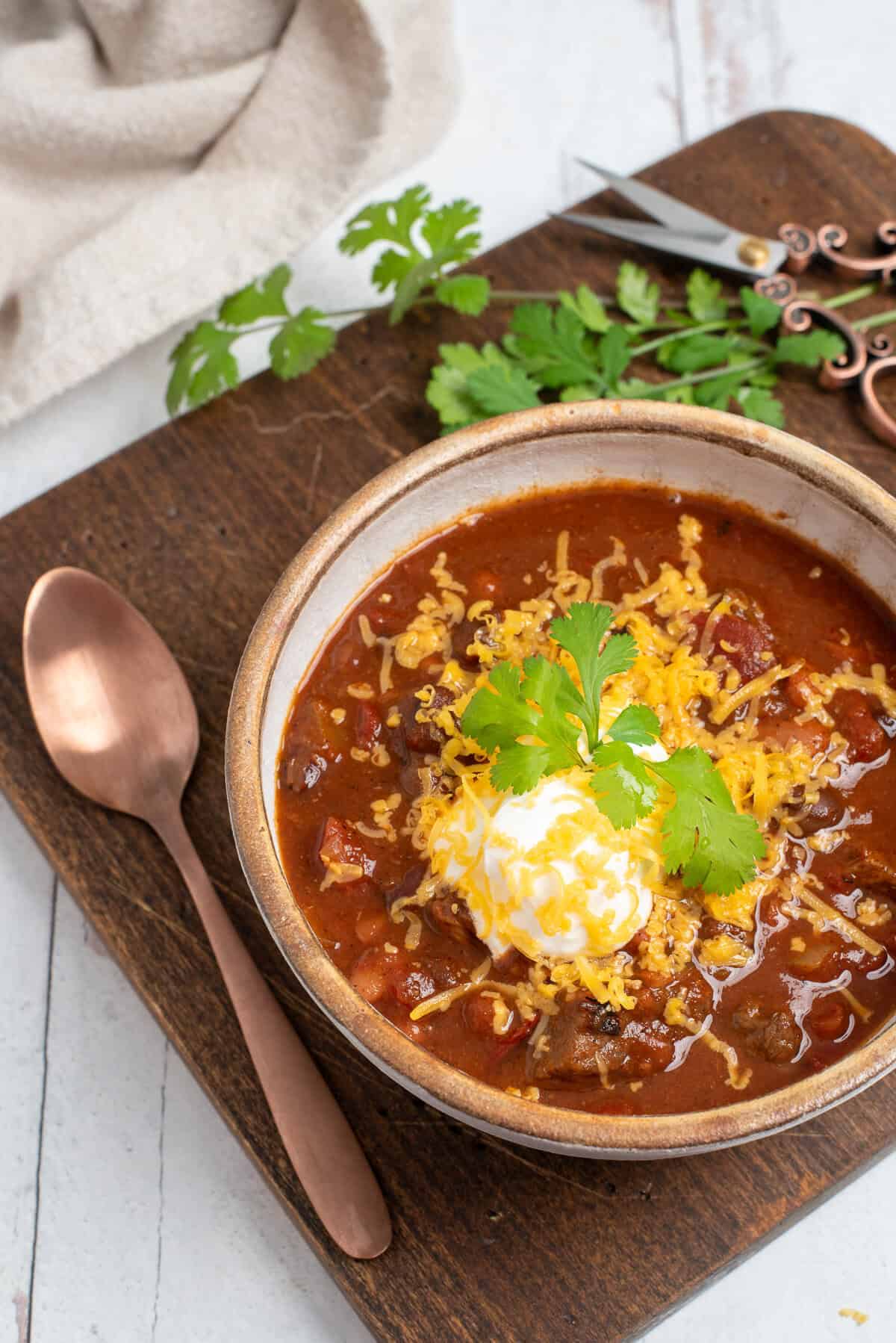 A bowl of chili topped with cheese, sour cream, and green onions.