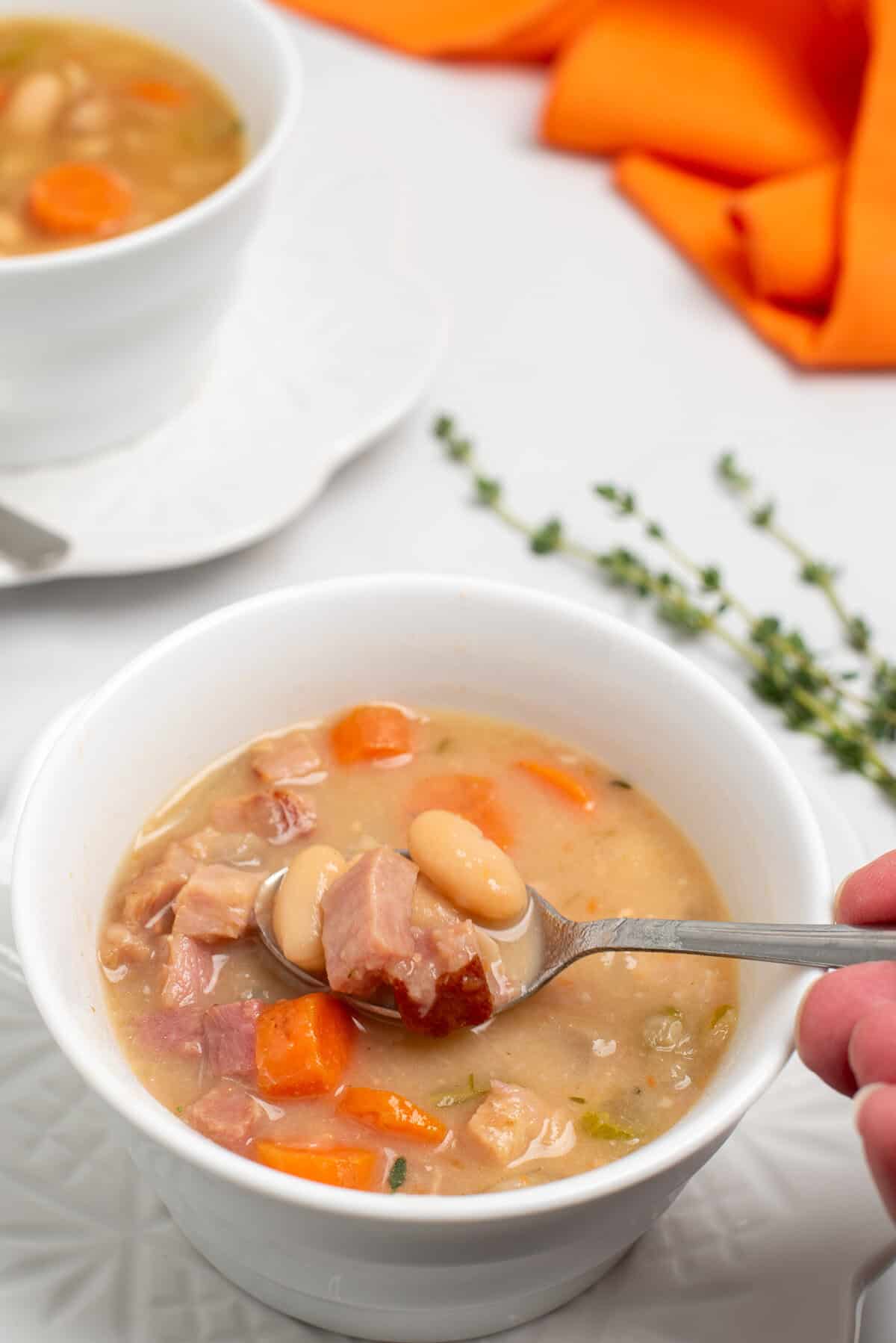 creamy bean soup with ham with a spoon lifting out a bite.
