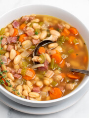 ham and bean soup in a white bowl with a spoon.