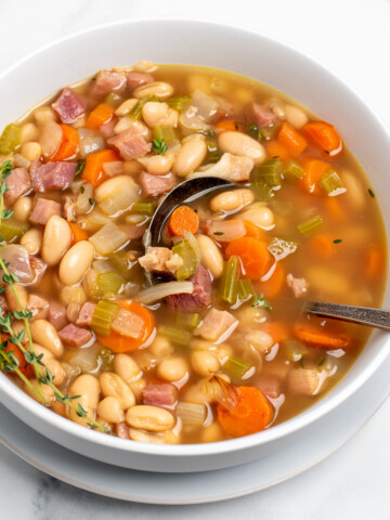 ham and bean soup in a white bowl with a spoon.