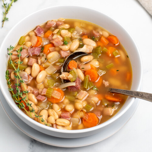 ham and bean soup in a white bowl with a spoon.