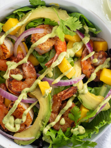 Shrimp Mango Salad in a white bowl topped with cilantro, lime, and an avocado lime dressing.