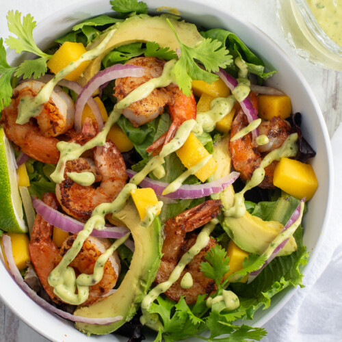 Shrimp Mango Salad in a white bowl topped with cilantro, lime, and an avocado lime dressing.