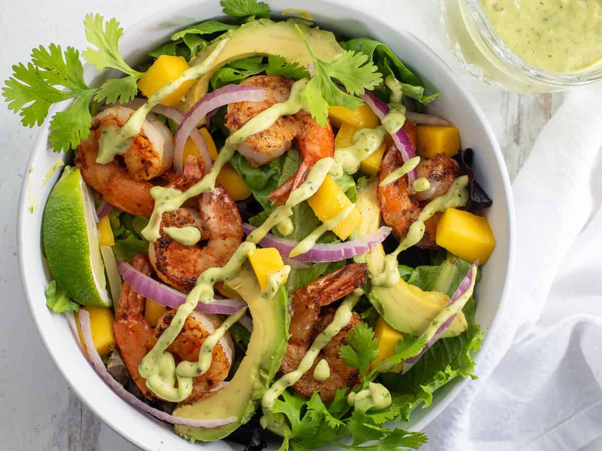 Shrimp Mango Salad in a white bowl topped with cilantro, lime, and an avocado lime dressing.