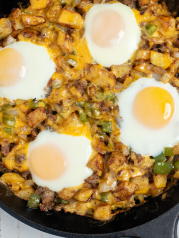 A breakfast skillet with sausage, topped with over easy eggs.