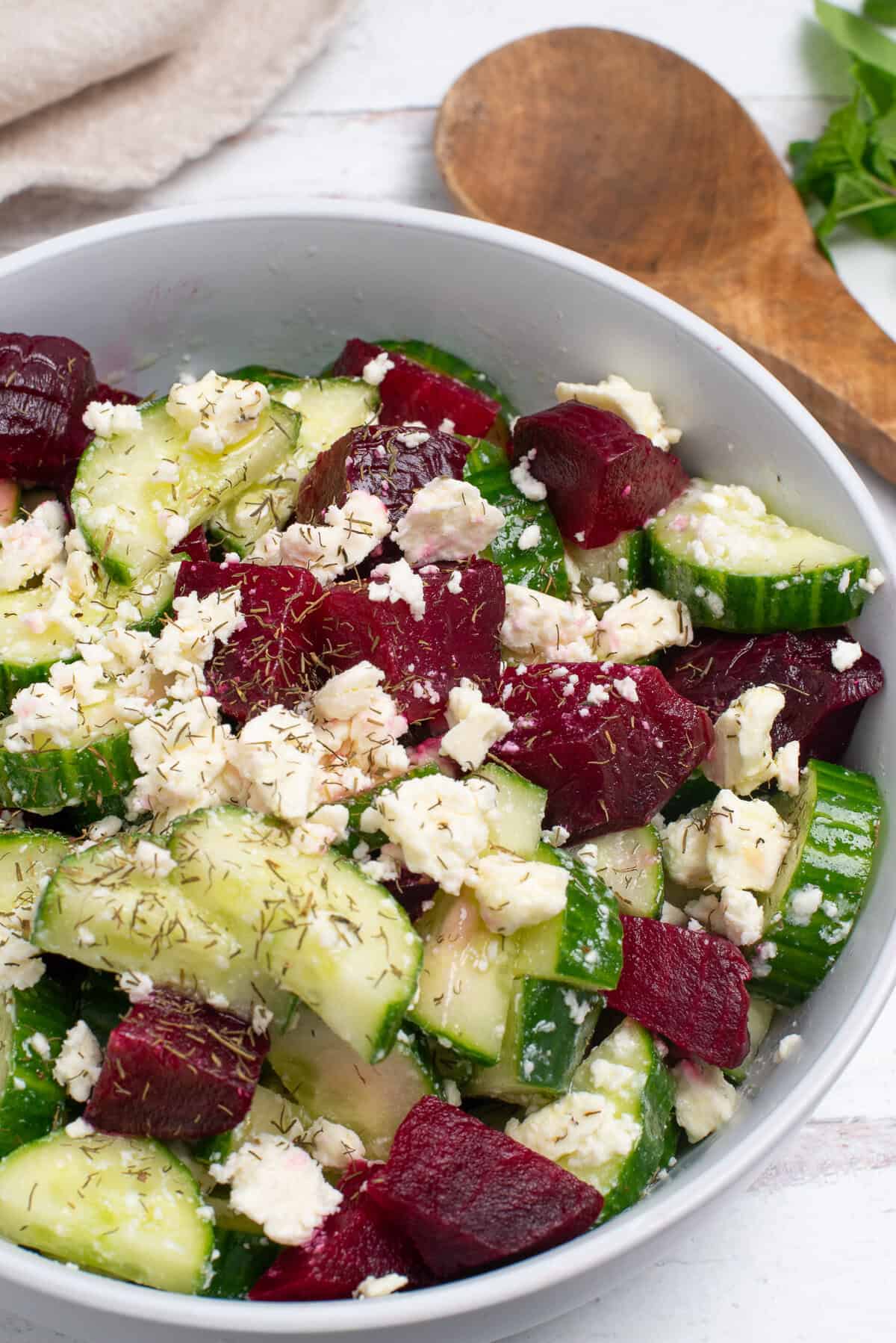 Beet cucumber salad in a bowl on a white table.