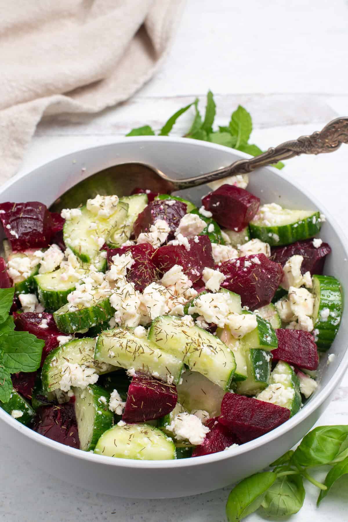 Beet cucumber salad in a white bowl with a spoon.