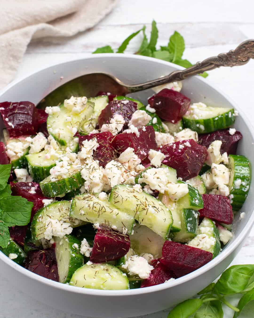 Cucumber and beet salad in a white bowl with a spoon.