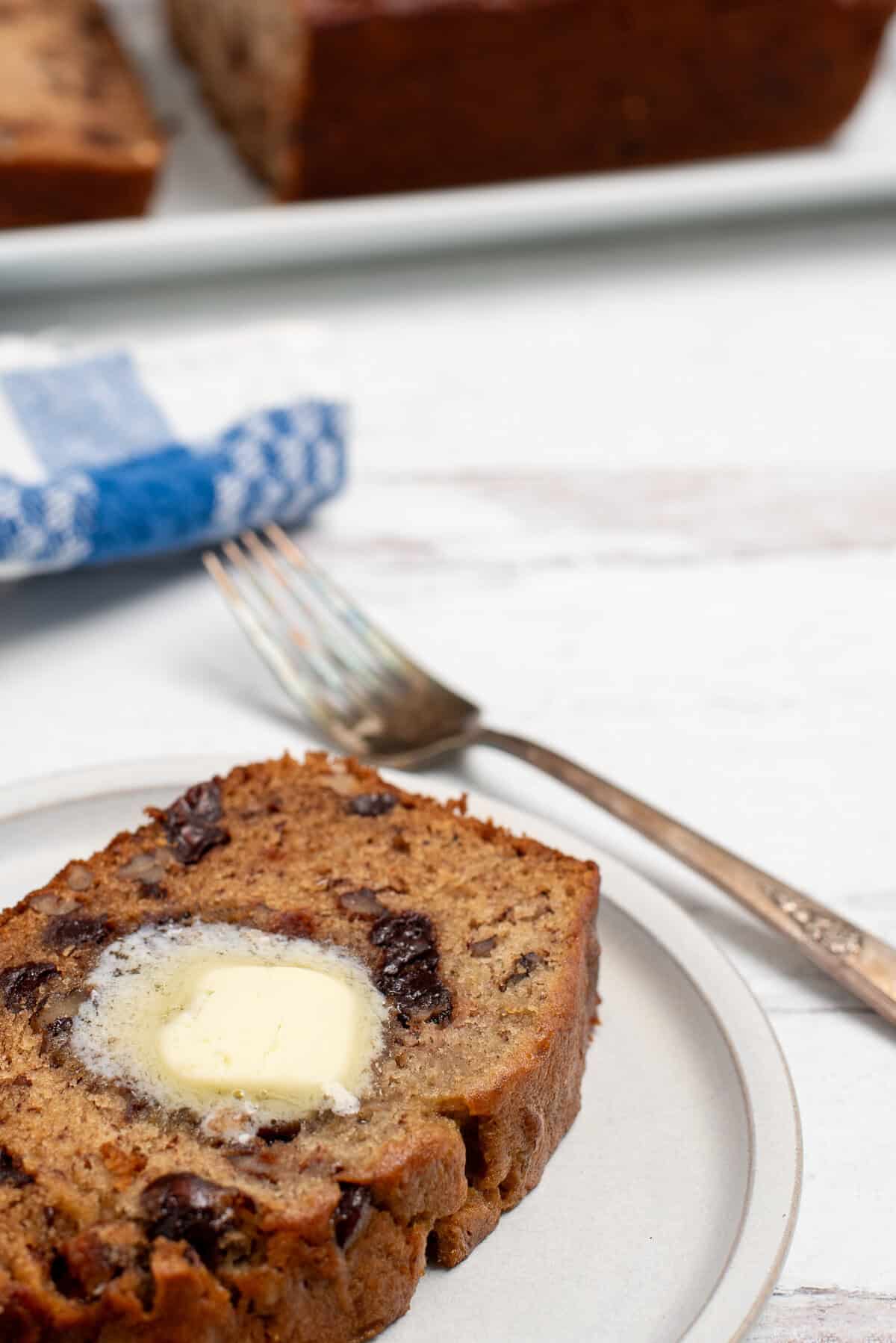 slice of banana nut bread with chocolate chips that has butter melted on top. 