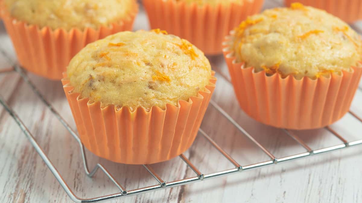 Banana carrot muffins on a wire rack with orange paper muffin liners.