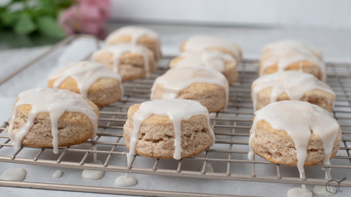 Cinnamon biscuits on a wire rack with glaze dripping off of them.