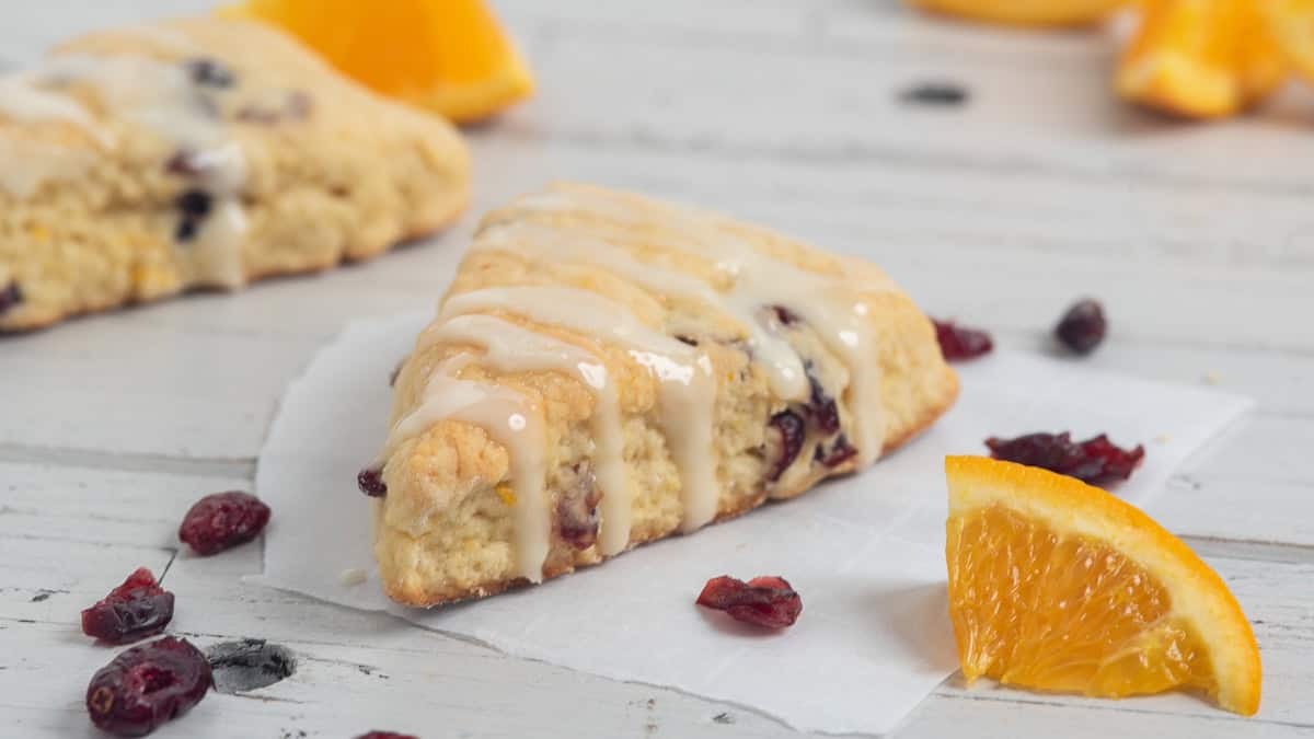 Cranberry orange scones on a white background with dried cranberries and orange slices scattered around.