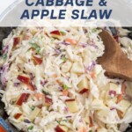 A dark bowl full of cabbage and apple slaw with a wooden spoon and a an orange napkin. The recipe title can be seen in text overlay.