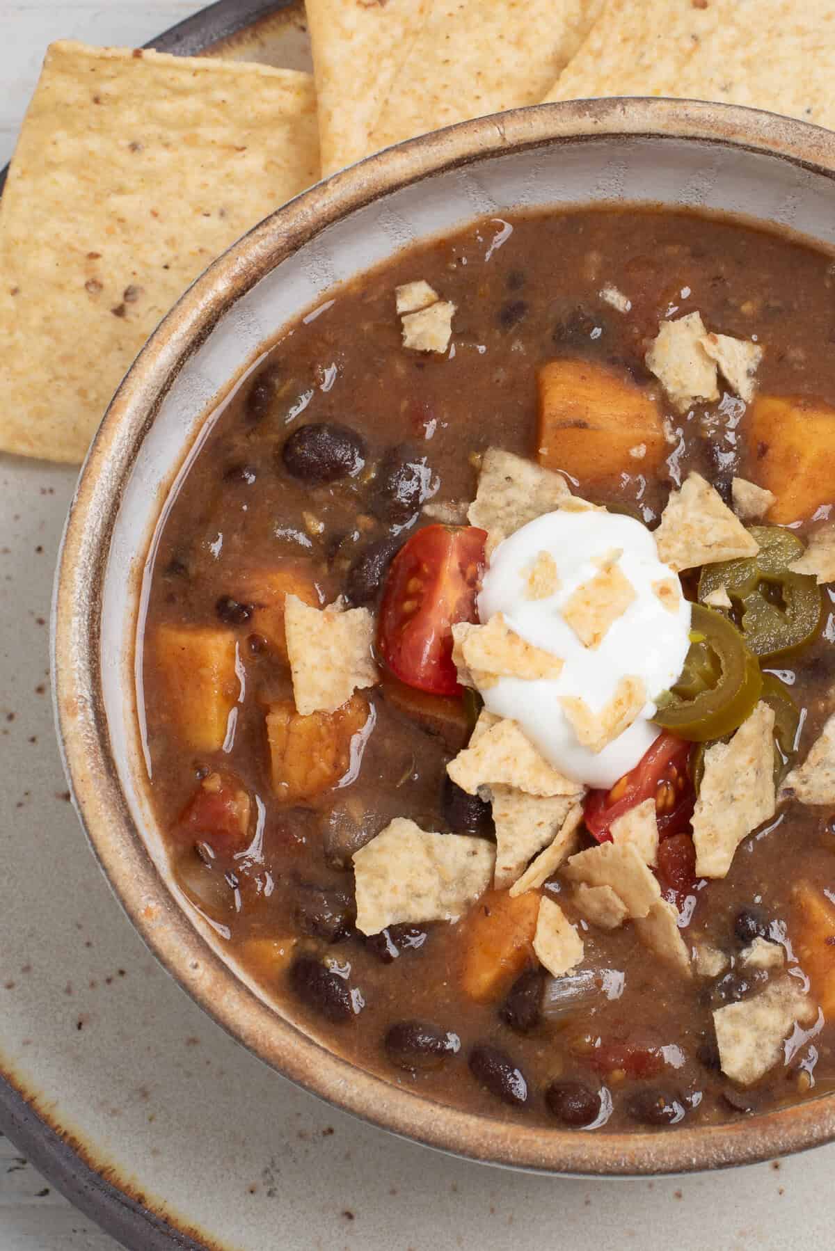 A bowl of black bean soup with sweet potatoes topped with sour cream, jalapenos, and crushed tortilla chips.