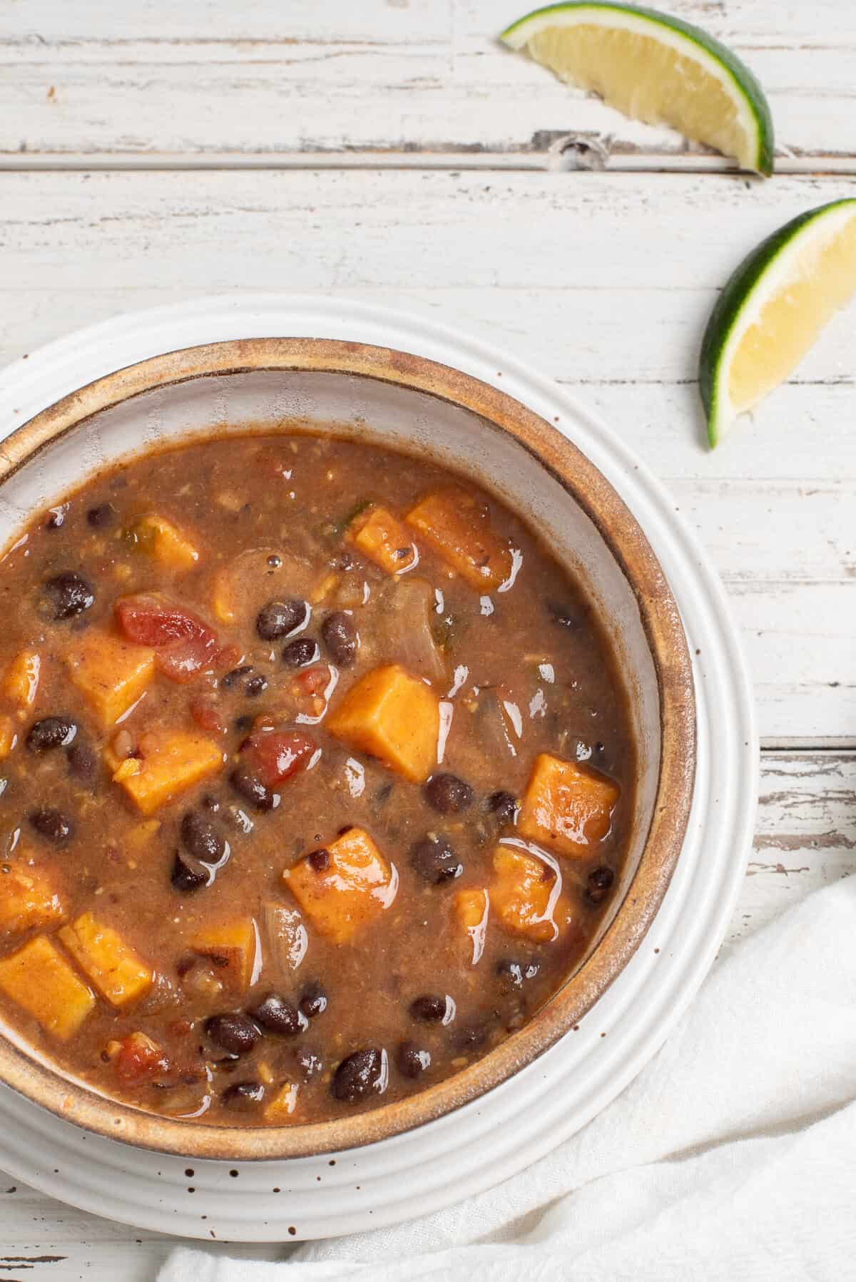 A bowl of sweet potato black bean soup on a white surface with a lime wedge nearby.